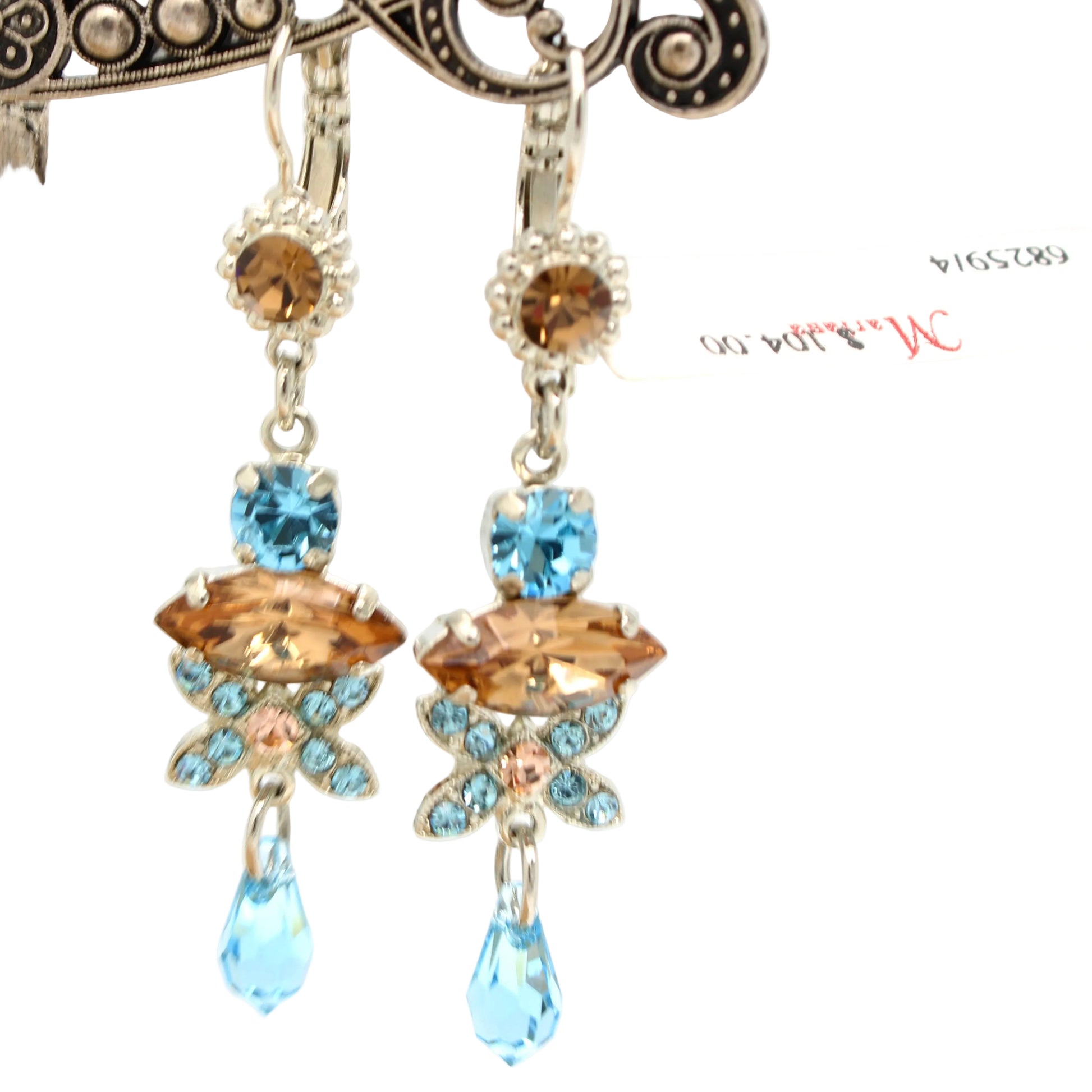 A pair of dangling statement earrings with silver-tone metal and faceted gemstones, featuring light blue marquise-cut stones, peach round stones, and a teardrop light blue stone at the bottom. A small white price tag is attached to the right earring.