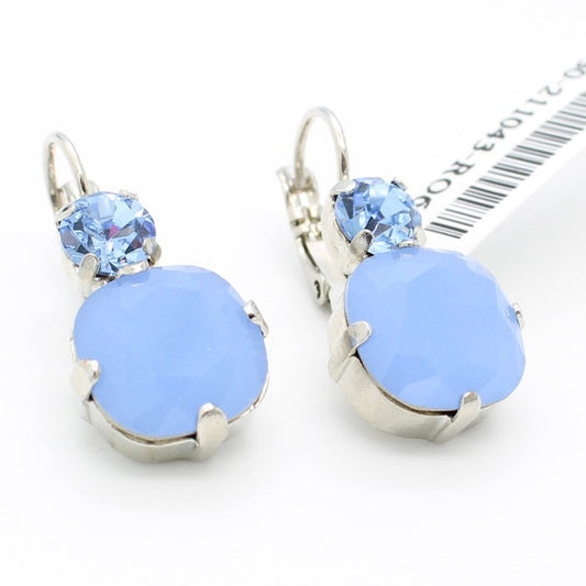 A pair of silver leverback earrings featuring a large light blue oval stone and a smaller round light blue crystal, displayed on a white background next to a barcode card.