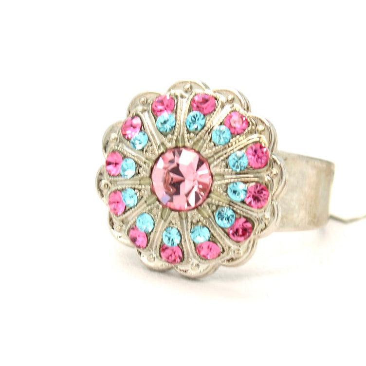 A silver-tone ring with a scalloped floral face featuring a large pink center stone and smaller pink and light blue stones around it, shown on a plain white background.
