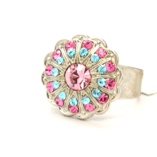 A silver-tone ring with a scalloped floral face featuring a large pink center stone and smaller pink and light blue stones around it, shown on a plain white background.