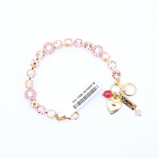 A gold-tone charm bracelet featuring pink and clear rhinestone flower charms, a gold heart-shaped lock charm, a pink bead, and a key-shaped charm engraved with 'Mia', shown on a white background with a product tag attached.